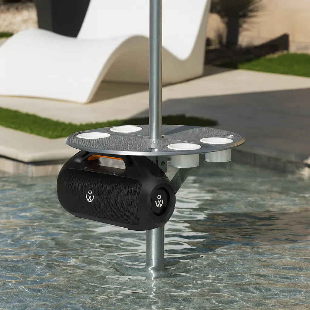 160W Bluetooth speaker Waterproof 160W portable speaker mounted under a BajaMate pool table, shown in a resort-style backyard setup with clear water and modern outdoor furniture.