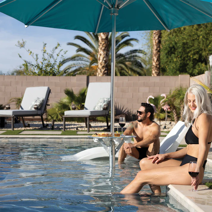 Couple enjoying the Baja Shelf Umbrella Table by BAJAMATE – luxury in-pool umbrella and table system by the poolside