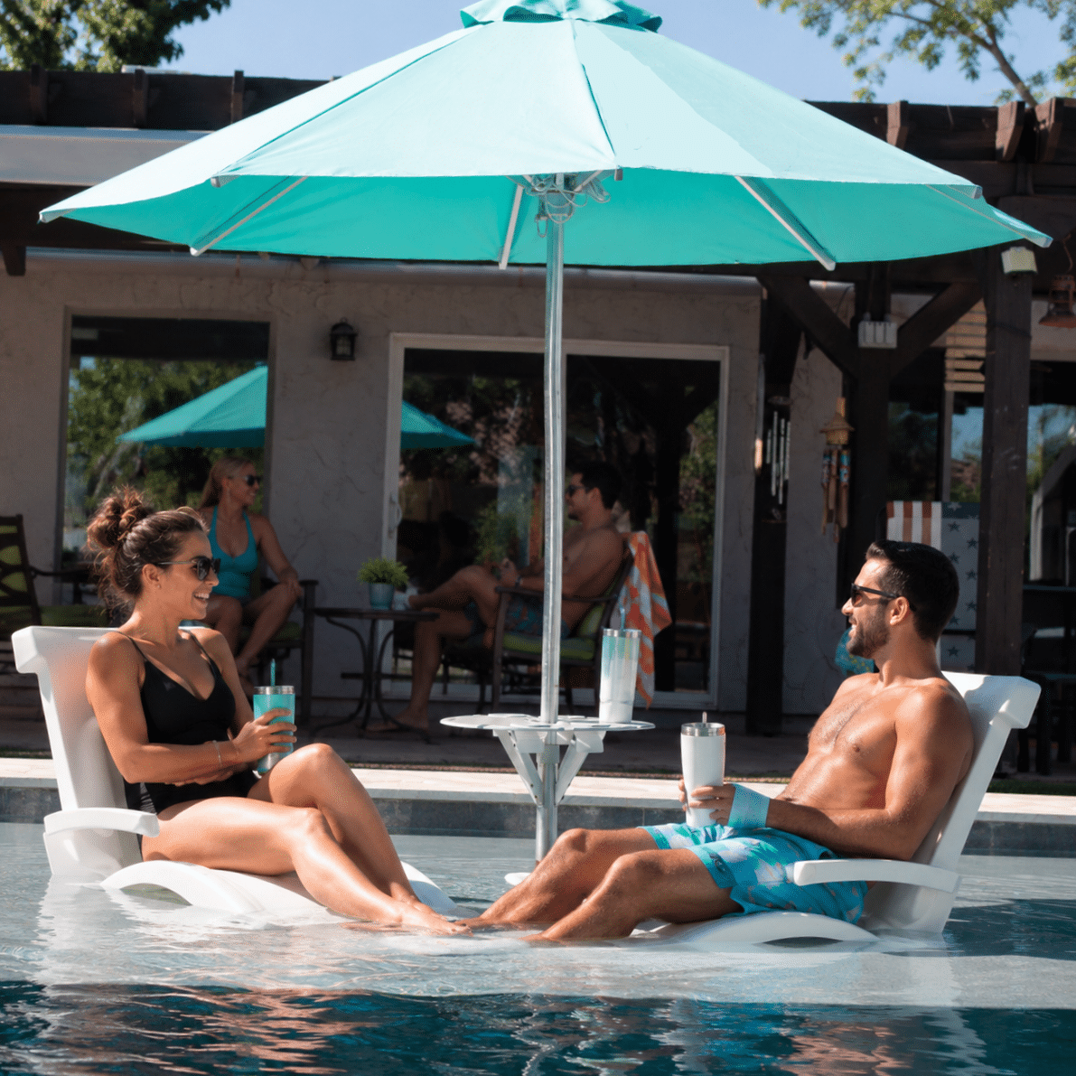 Turquoise pool umbrella with a centered BajaMate table between two white in-pool lounge chairs on a sunny backyard pool shelf.